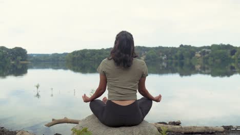 mujer latina sentada en pose de meditación junto al agua