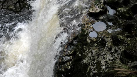 Langsamer-Schwenk-über-Den-Wasserfall,-Der-Sich-Schnell-über-Braune,-Moosbedeckte-Felsen-Mit-Pfützen-In-Einer-Natürlichen,-Rauen-Wildnis-Ergießt-Und-Spritzer-Und-Blasen-Im-Fluss-Erzeugt