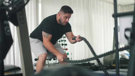 hombre que usa cuerdas de batalla para hacer ejercicio en un gimnasio
