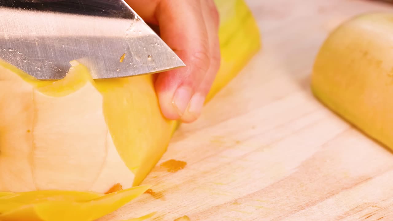 Detailed view of hands slicing butternut squash on a wooden board using a sharp knife.