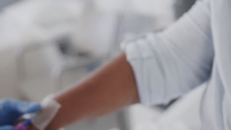 una mujer médica diversa tomando una muestra de sangre de una paciente de edad avanzada en una cama de hospital, en cámara lenta.