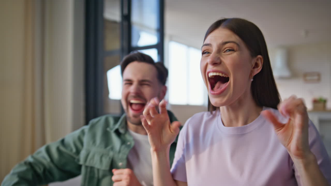 Closeup emotional fans cheering sport sitting couch. Two people celebrating win