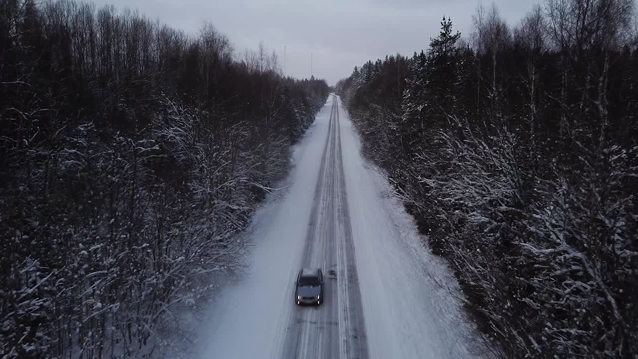 vista aérea del callejón de la carretera de invierno rodeado de árboles cubiertos de nieve en un día de invierno nublado, pequeños copos de nieve cayendo, conducción de automóviles a través de un gran ángulo de tiro de drones ascendentes lentos moviéndose hacia atrás