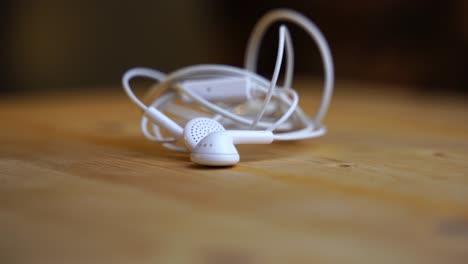 white in ear headphones with cable and aux plug lies on a light wooden board and rotates