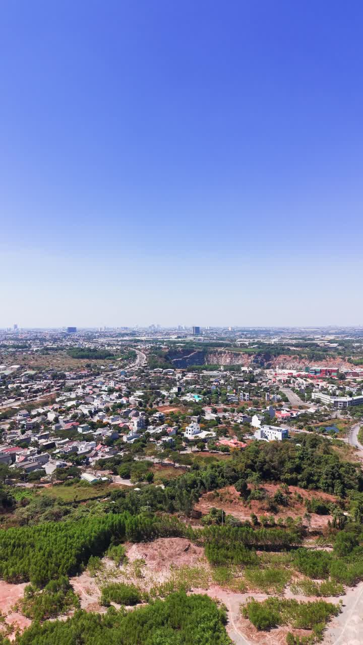 Vista del paesaggio urbano con colline verdi e uno specchio d'acqua in una giornata limpida nel pomeriggio, da un punto elevato vicino a una strada locale.