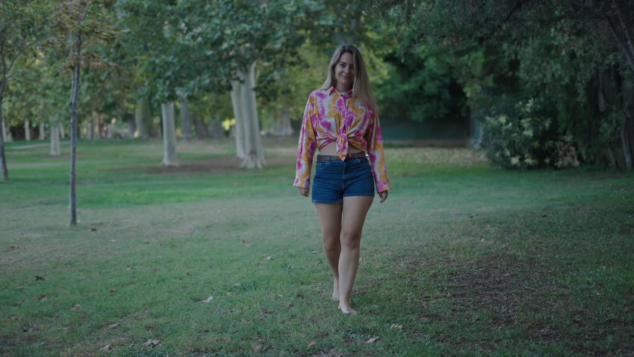 Woman walking barefoot in a park wearing tie-dye shirt and shorts.