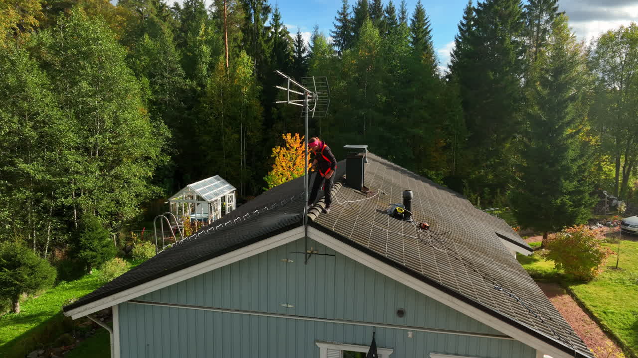 Aerial view orbiting a woman washing house roof tiles, sunny, fall day in Finland