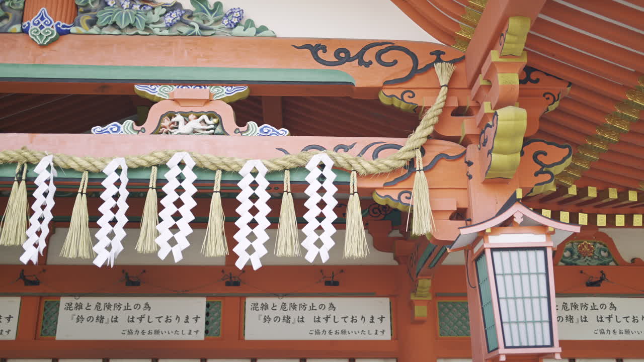 A vibrant shrine entrance featuring intricate wooden carvings and traditional decorations. Translation of text: ''Ring bell has been removed for safety''. Fushimi Inari, Kyoto, Japan