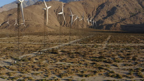 stunning aerial view of drone flying backwards alongside many wind turbines with huge mountain in the background at wind farm near palm springs in the mojave desert, california, usa