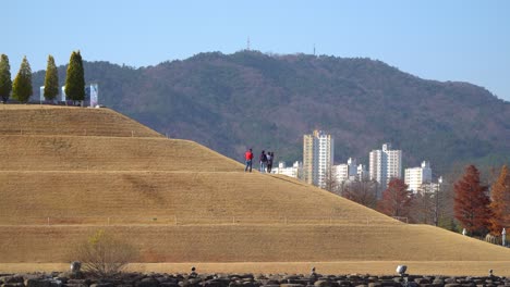 visitors strolling up the bonghwa hill on a spiral road in lake garden of suncheonman bay national garden with suncheon city buildings and mountains on background