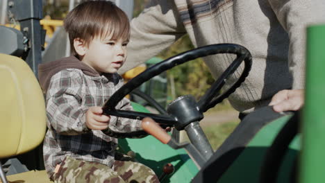 a farmer shows his young son a tractor, a toddler playing behind the wheel