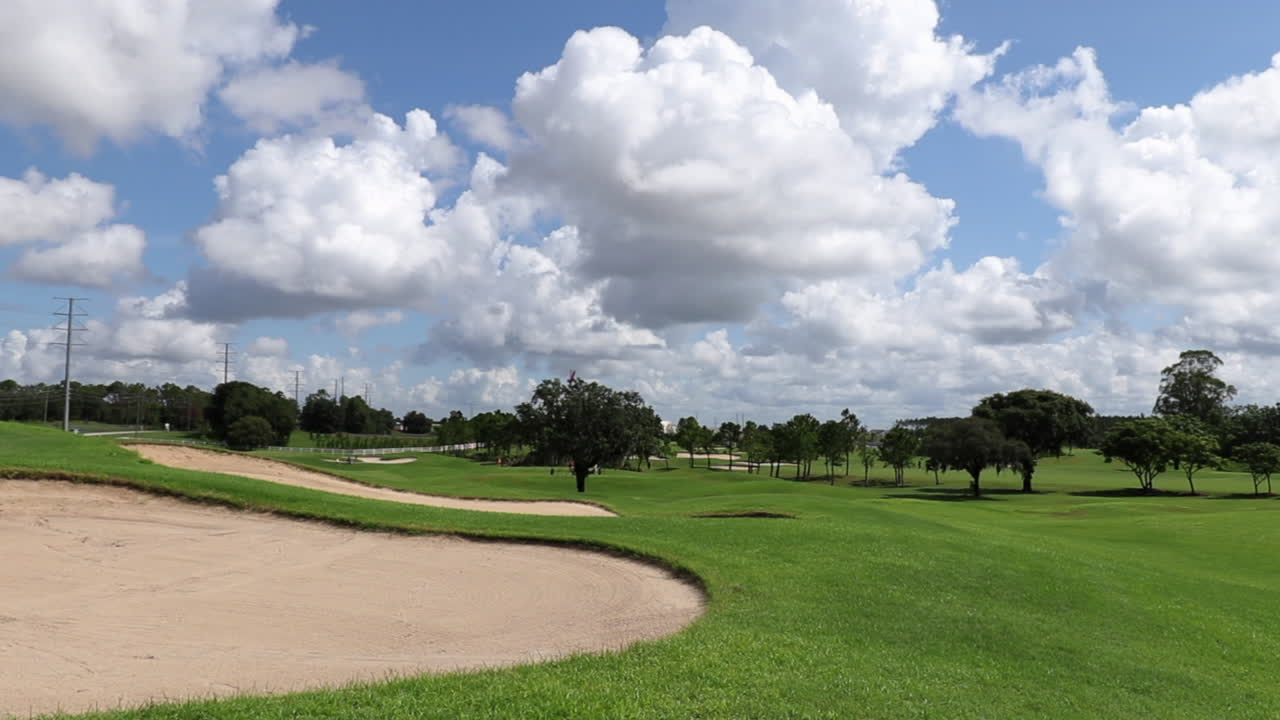 paisaje de un gran campo de golf que muestra hierba verde y areneros y árboles a lo lejos del campo de golf