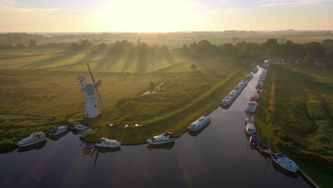 Aerial-footage-of-Thurne-Mill-on-the-Broads-in-Norfolk-Uk-with-the-camera-rotating-around-the-mill-at-sunrise-with-mist-and-sun-rays-shining-across-the-fields