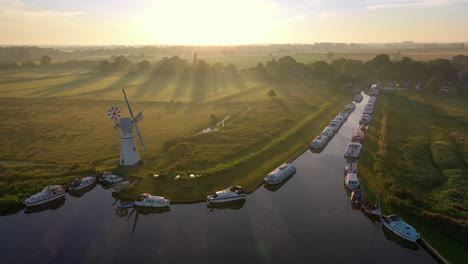 aerial footage of thurne mill on the broads in norfolk uk with the camera rotating around the mill at sunrise with mist and sun rays shining across the fields