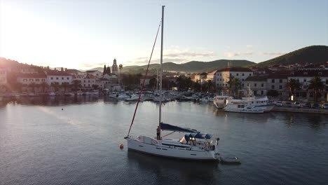 Stetige-Drohnenaufnahmen-über-Hafengewässern-In-Mittlerer-Höhe-Mit-Segelboot-Und-Dorf-Im-Hintergrund