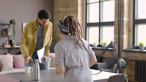 Young-Man-And-Blonde-Woman-Sitting-At-A-Table-With-Microphones-And-Computer-To-Recording-A-Podcast