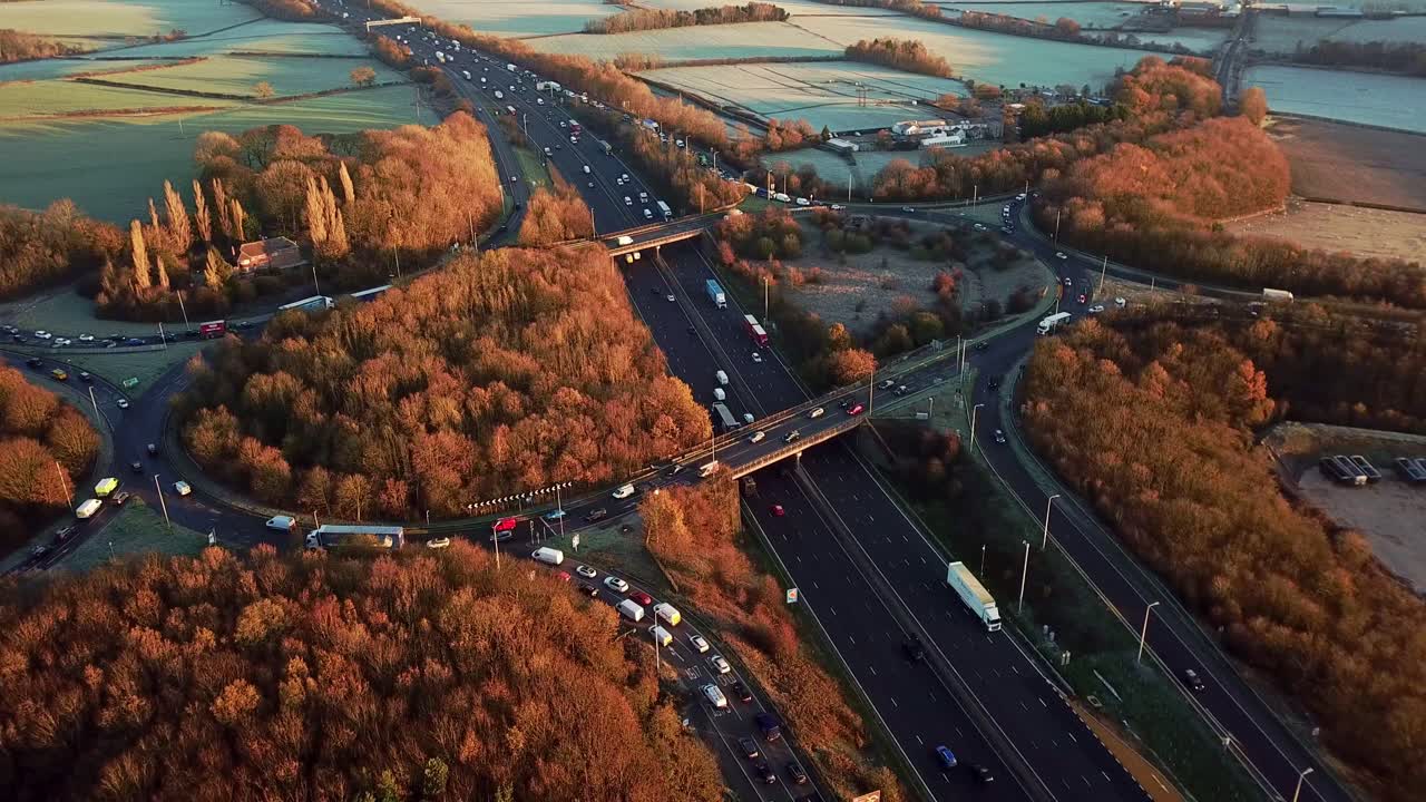 Drone Aerial View Of A Busy Motorway Junction Flying Backwards Out With Cars And Trucks In The Winter With Orange And Brown Trees