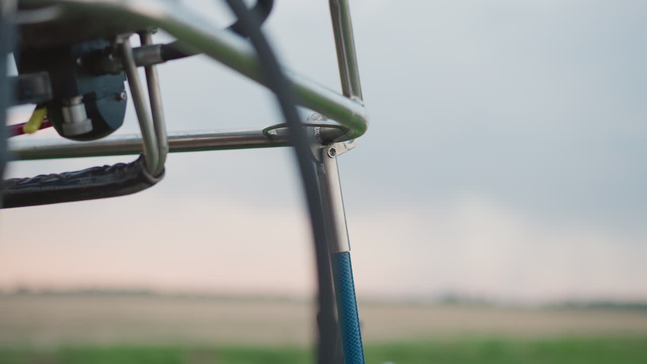 gloved hand adjusting hook and securing burner frame joint during hot air balloon preflight setup over grassy field under cloudy sky with focus on metal rod connection and rigging detail
