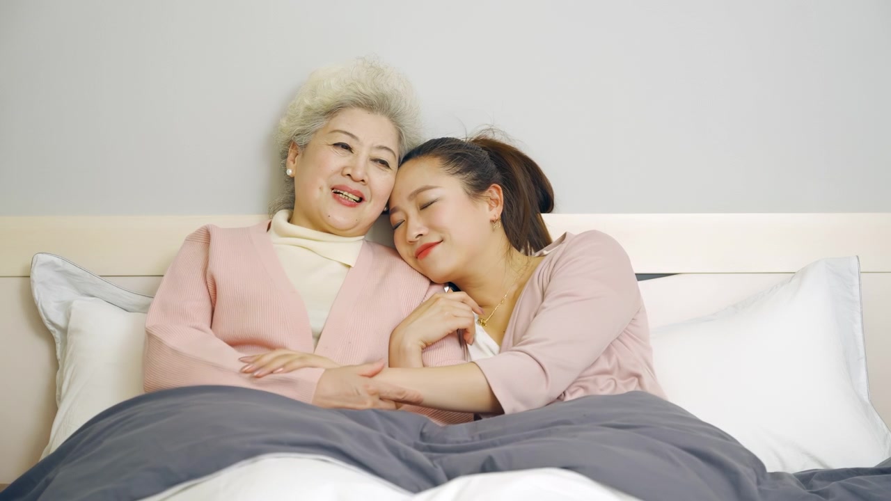 喜びに満ちた高齢の祖母、母親、そして成長した娘がベッドで抱き合い、寄り添いながら、楽しく心地よい会話を交わしています。家族の絆を深め、秘密を共有する週末の訪問です。