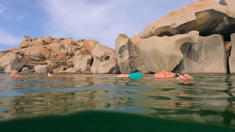 escena medio submarina de mujer en bikini azul relajándose flotando en el agua de mar de la bahía de cala della chiesa con rocas graníticas erosionadas en el fondo de la isla lavezzi en córcega, francia