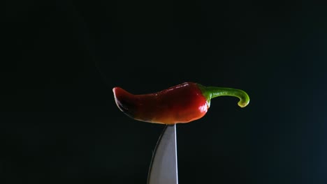 un jalapeno fumador en la punta de un cuchillo con un fondo oscuro