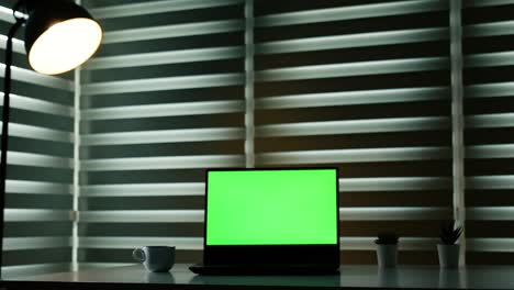 laptop with green screen on white table in front of roller blind. with coffee fog. dolly in