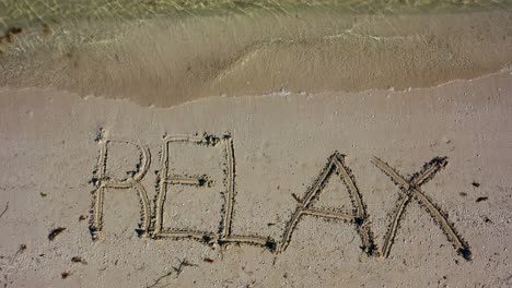 static shot of relax written in the sand