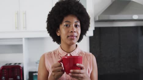 portrait of african american woman holding coffee cup and smiling in the kitchen at home