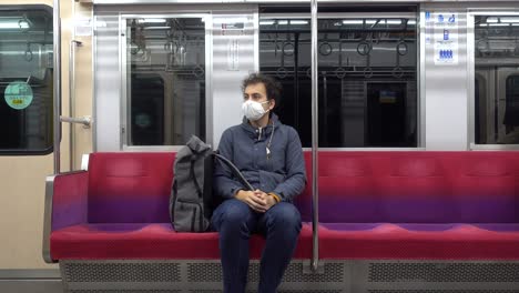 hombre solitario con una máscara facial sentado dentro de un tren brillante durante la crisis de la corona