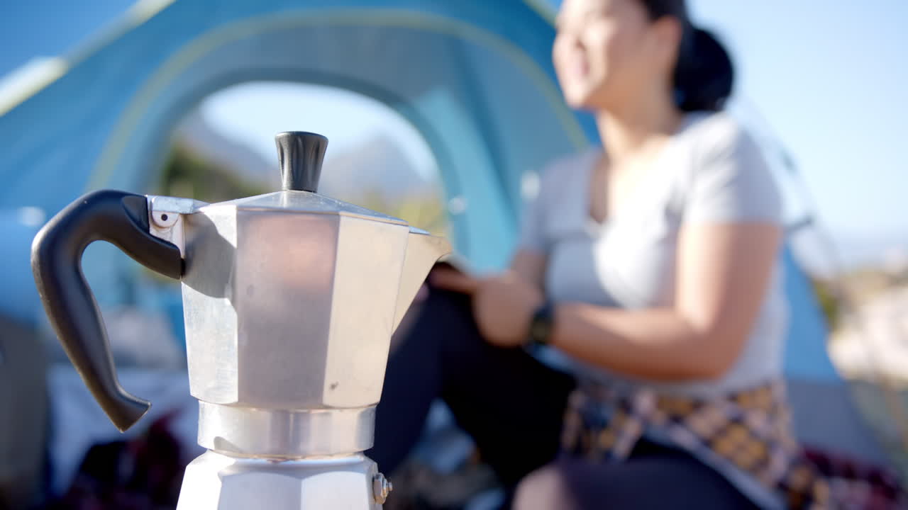 Camping in mountains, woman sitting by tent and writing in notebook