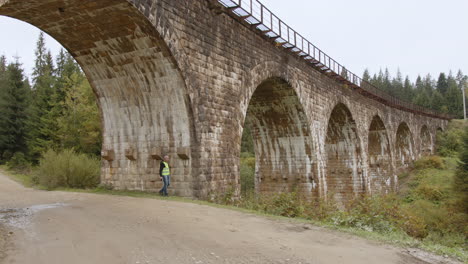 engineer inspecting an old stone arch railway bridge in a forest