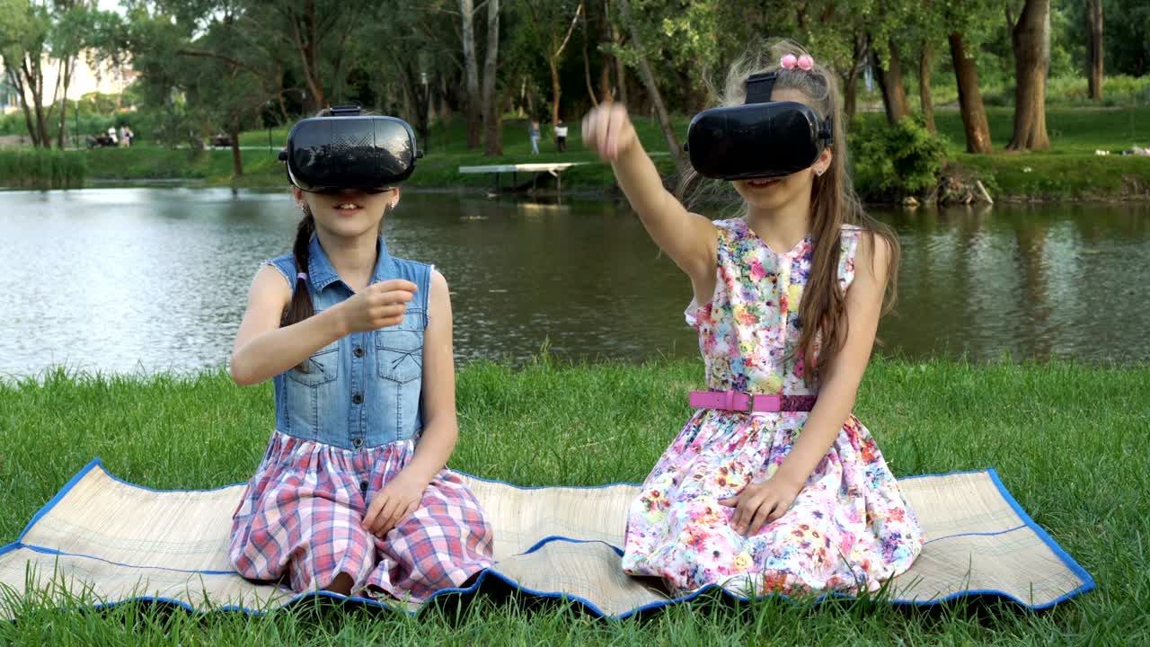 아이들은 가상현실 안경으로 공원에서 강변의 잔디에 앉아 가상 게임을 하며 손을 흔들고 웃는다.