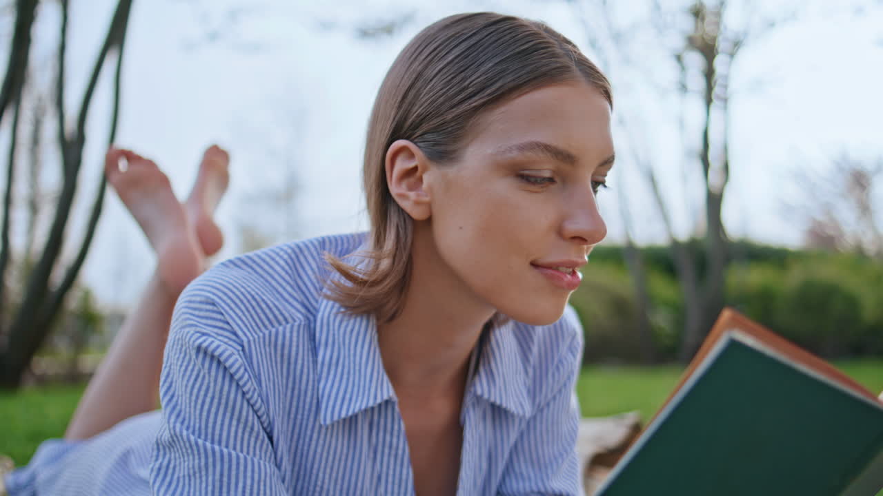 Smiling girl reading romance lying on park grass closeup. Lady looking camera
