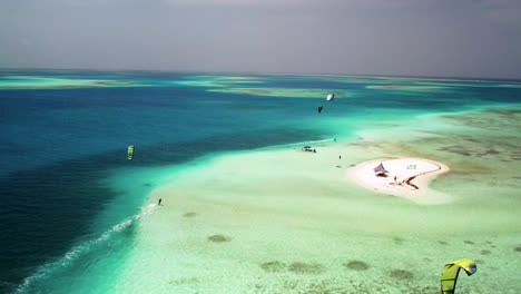 Kite-surfers-near-sardina-island-with-vibrant-turquoise-waters-and-sandy-beach,-aerial-view