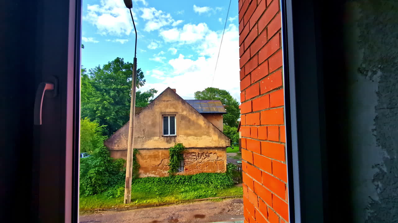 Old rustic house overgrown with ivy seen through window frame from dark room