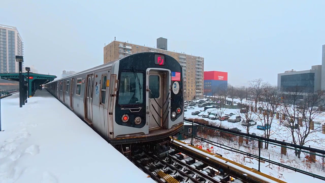 New York, USA, 25 dicembre 2025: Treno F su una banchina coperta di neve, New York City. Vagone della metropolitana fermo con porte chiuse, adesivo con bandiera e binari innevati.