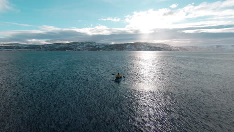 Man-paddling-on-blue-kayak-towards-sun,-enjoying-the-scenery