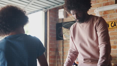 Middle-aged-black-father-and-his-pre-teen-son-shake-hands-to-celebrate-the-completion-of-a-racing-kart-they-built-together-in-their-garage,-low-angle