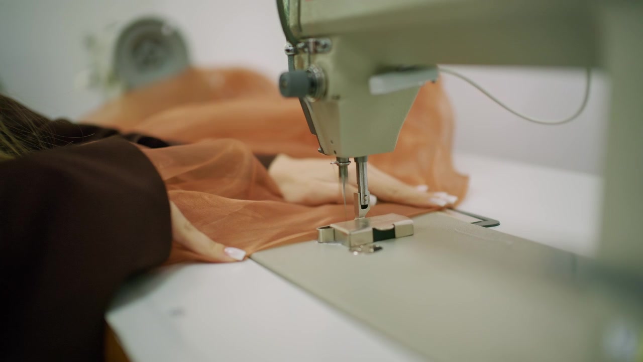 Close up of a person guiding brown sheer fabric under the needle of an industrial sewing machine