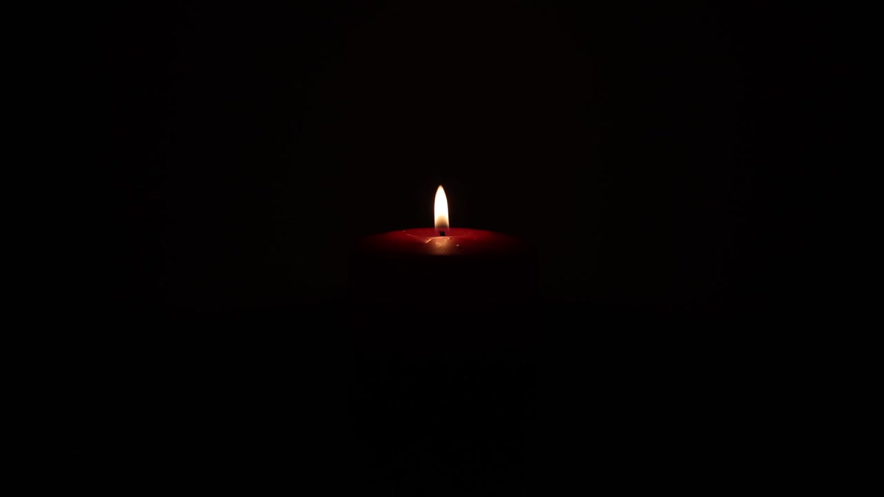 La fiamma di una singola candela tremola in una stanza buia