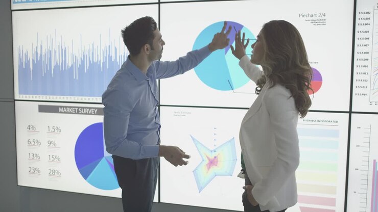 Businessperson meeting in boardroom referencing spreadsheet data on big screen