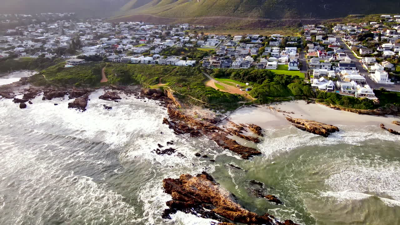 drone tilt-up sobre la costa de hermanus revela el vecindario de voëlklip bajo la montaña