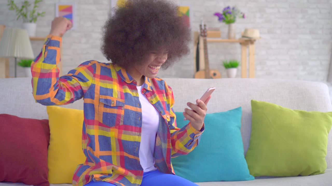 una alegre mujer afroamericana con un peinado afro usa un teléfono inteligente y se enteró de la victoria