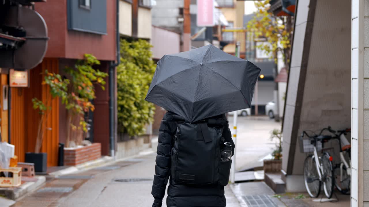 A woman strolls through the charming streets of Takayama on a rainy day, her umbrella shielding her from the gentle drizzle.