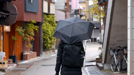 a woman strolls through the charming streets of takayama on a rainy day, her umbrella shielding her from the gentle drizzle.