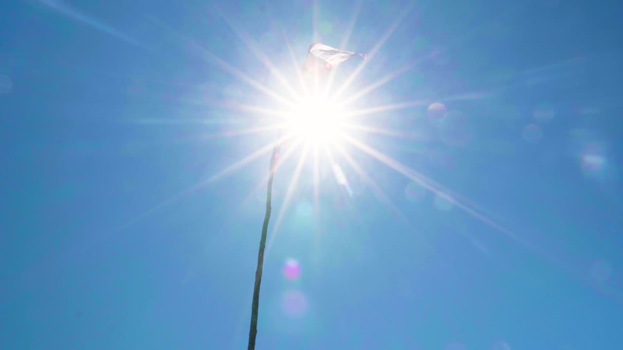 Handheld of sun beams shining through chilean flag hoisted on a pole and waving in the wind at daytime