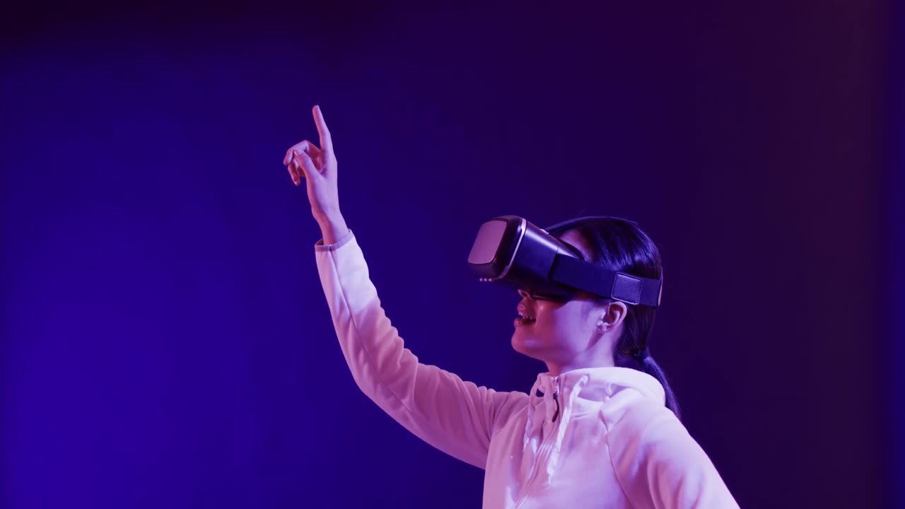 Asian woman using vr headset, touching virtual screen on blue background, copy space, slow motion