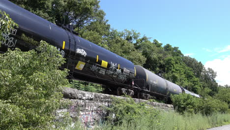 railroad tanker cars, tagged with graffiti, sit idle on an elevated siding or spur