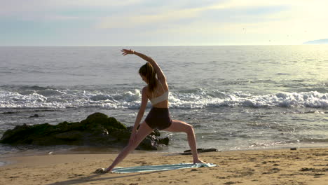 una atractiva joven practicando yoga en una hermosa playa de california