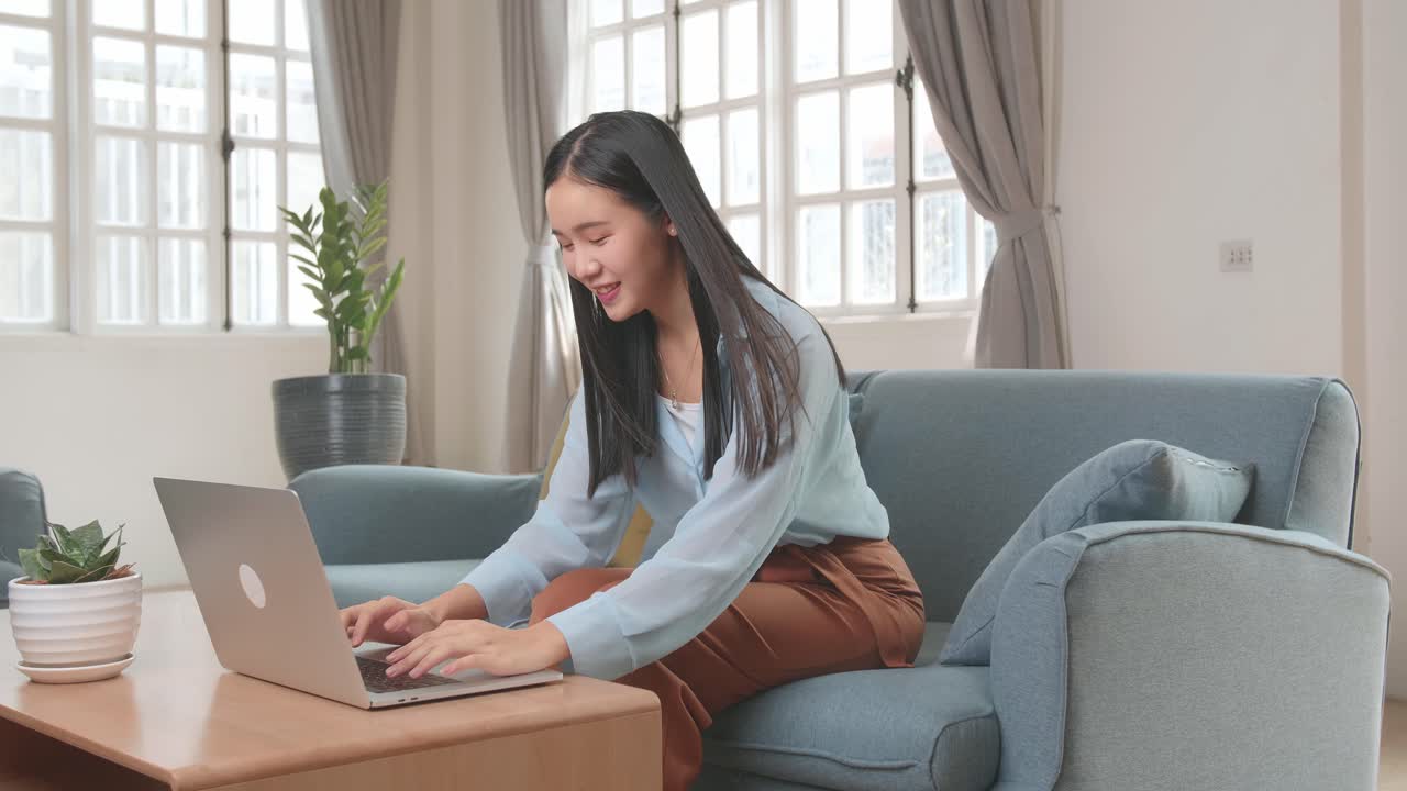 Asian Female Working On Laptop And Smiling At Living Room While Sitting On Sofa, Video In 4K